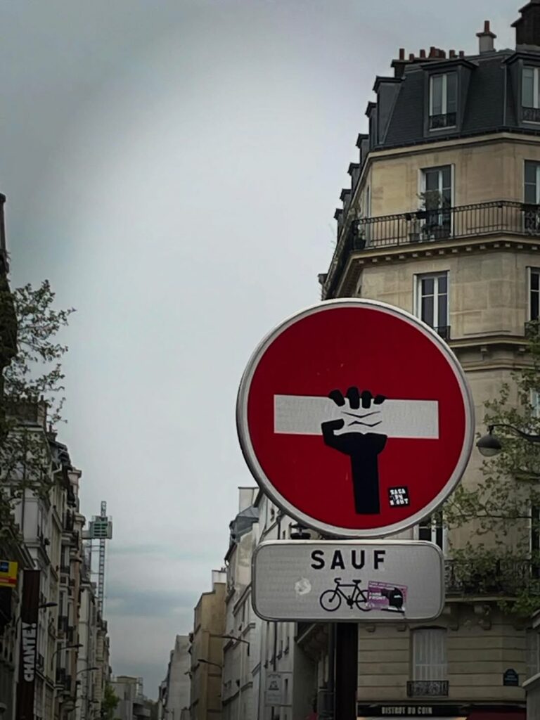 panneau sens interdit sur lequel un bras de travailleur brandit la barre blanche horizontale serrée dans son poing levé