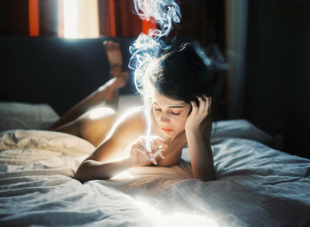 allongée sur son lit, une femme lumineuse fume une cigarette